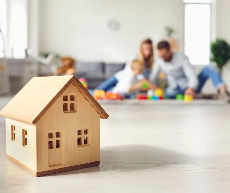 small wooden house in forefront of picture with a family sitting in the background