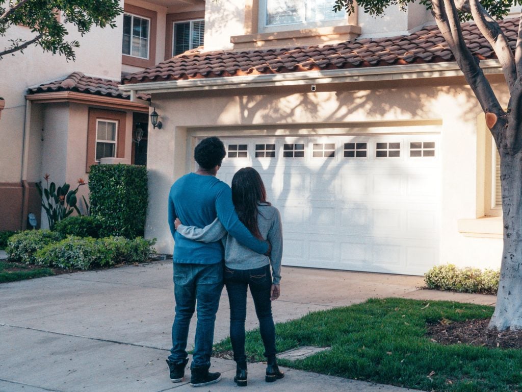 Young couple with their arms around each other standing in front of and looking at a house