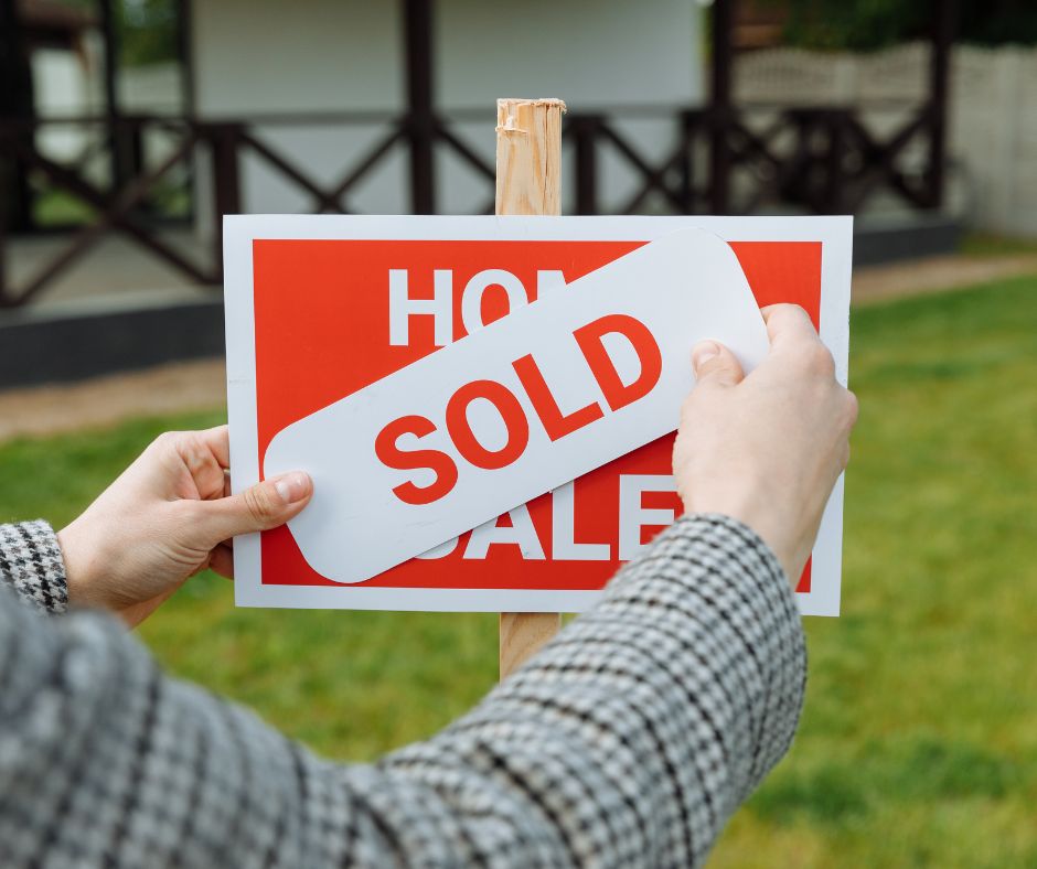 picture of a for sale sign with a person placing a sold sign over it